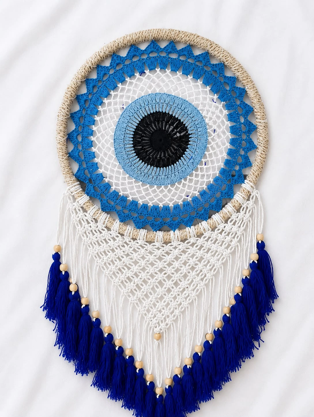 Round macramé evil eye wall hanging with woven blue and white eye design, jute-wrapped hoop and navy blue tasseled beaded fringe